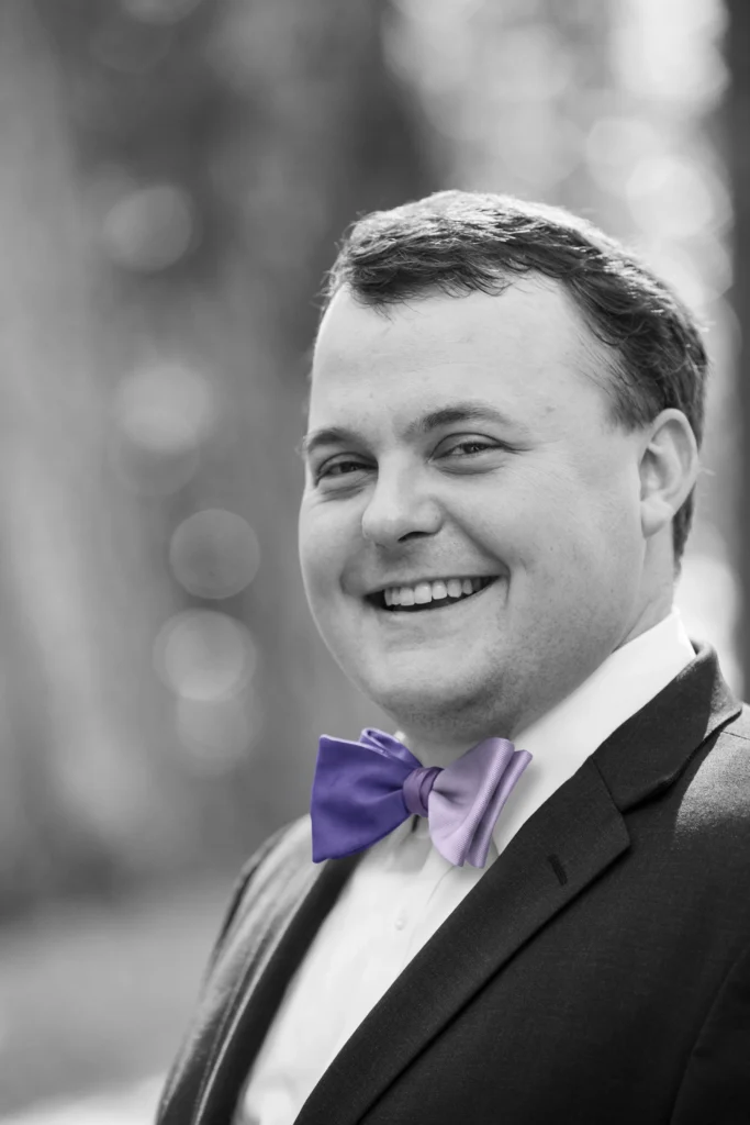 Black-and-white portrait of a smiling man wearing a dark suit and purple bow tie.